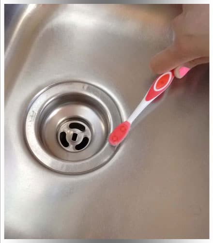 Professional cleaner cleaning drain with pink toothbrush