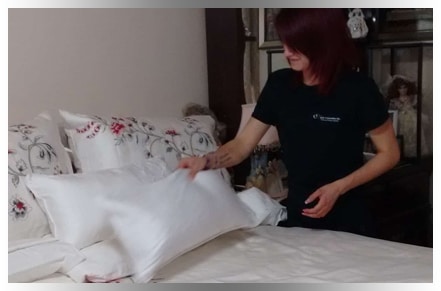 Young red-haired cleaning professional placing pillow on clean bed sheet
