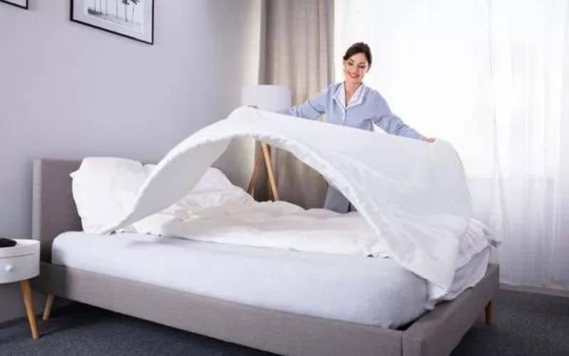 A lady changing sheets of bed