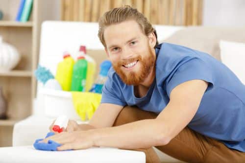 Smiling bearded cleaner spraying fabric ottoman