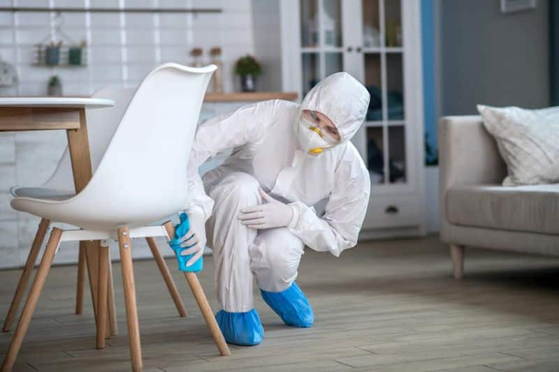 Professional cleaner with mask and protective suit wiping chair leg