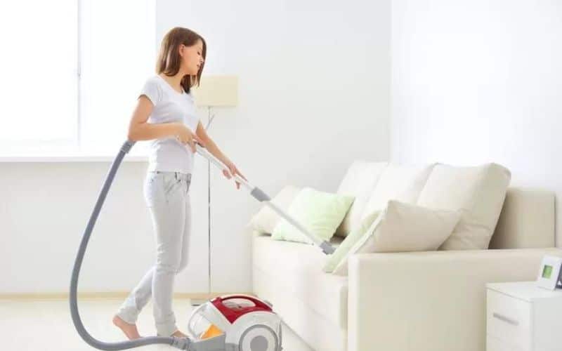 A Woman Cleaning the Couch using a Vacuum Cleaner